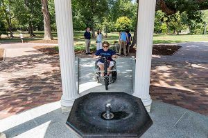 Student in motorized wheelchair rolling up Old Well pathway